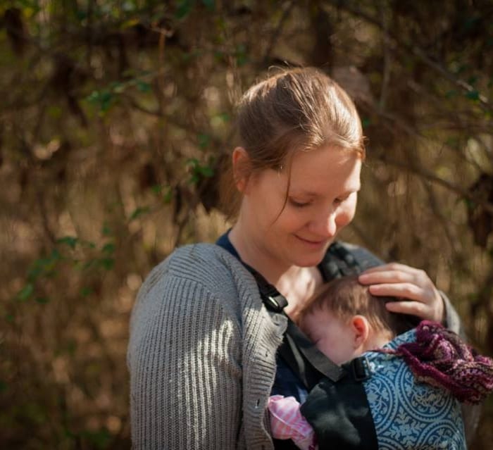 Mother babywearing infant in a carrier outdoors